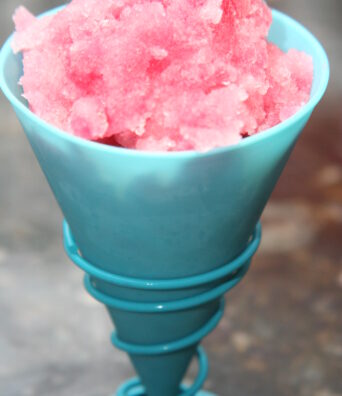 Reddish pink Hawaiian shave ice is served in a plastic cone.